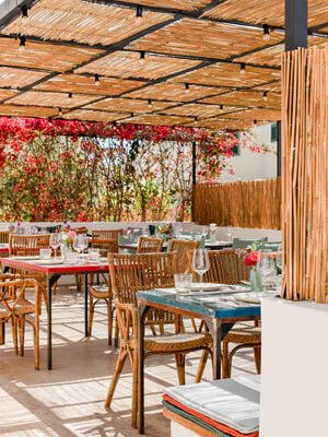 La terraza del restaurante es sombreada, con un tejado de flores, un acogedor banco de piedra con muchos cojines de colores y mesas puestas.