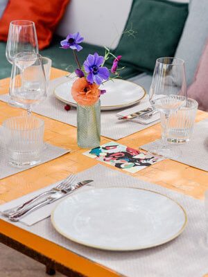 Detail of a beautifully laid orange tiled table with floral decorations and Mediterranean illustrations on the menus.