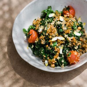 White ceramic plate showing the grilled kale salad with quinoa and cherry tomato confit.